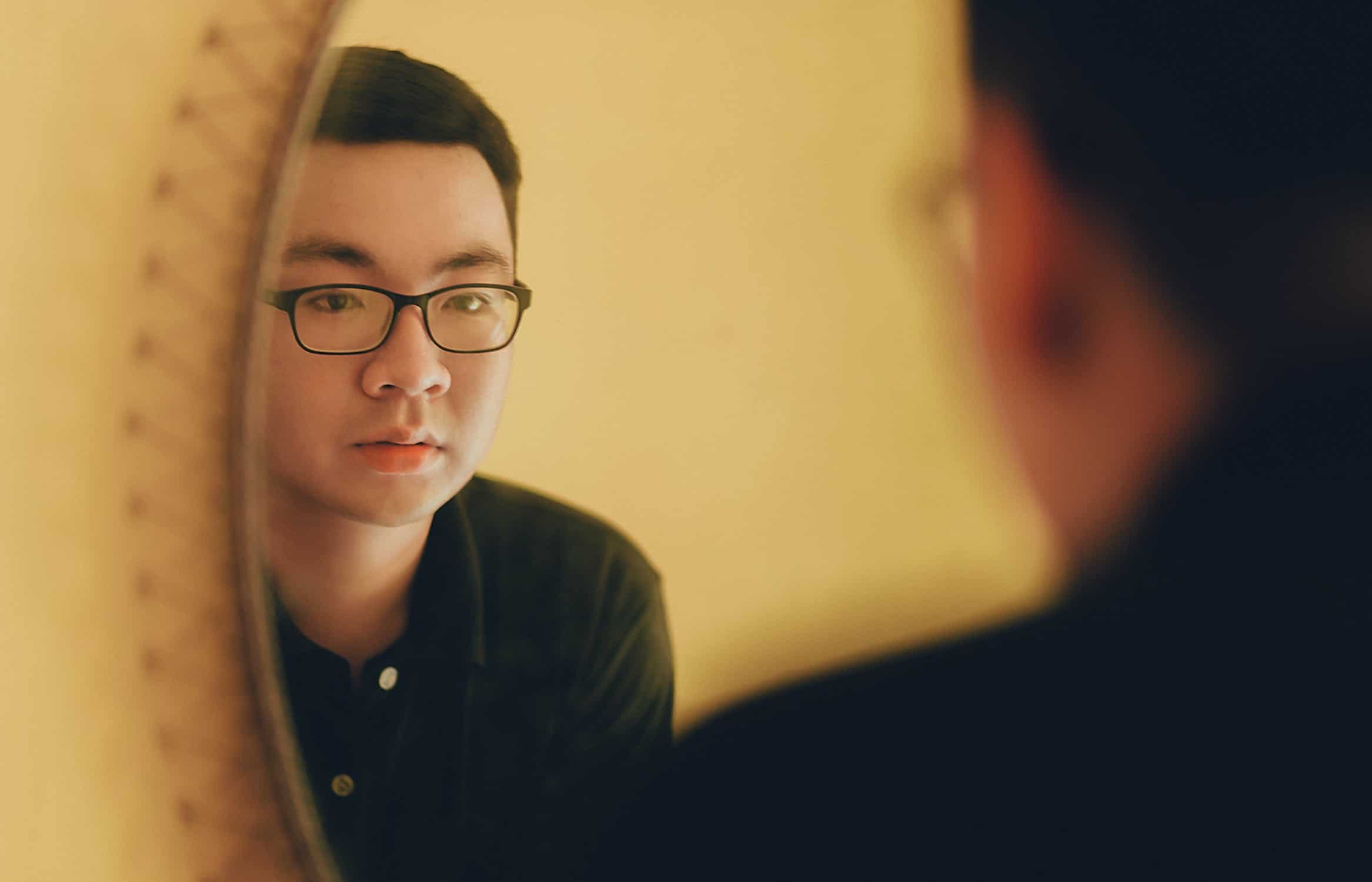 man with glasses looking at himself in the mirror