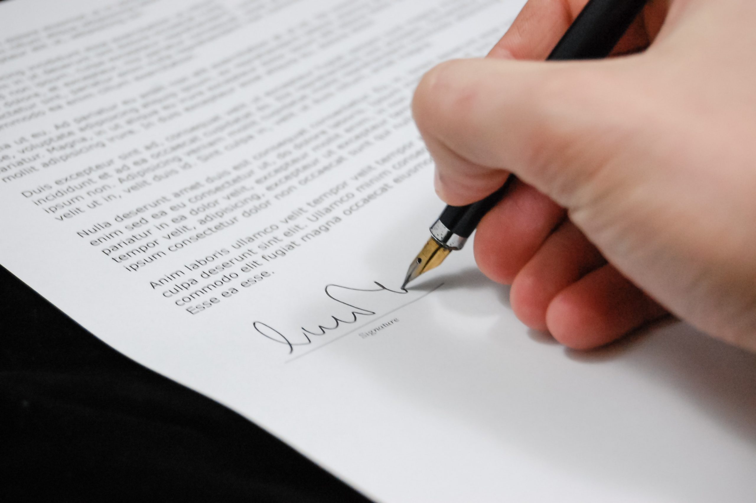 hand signing a document with a black pen