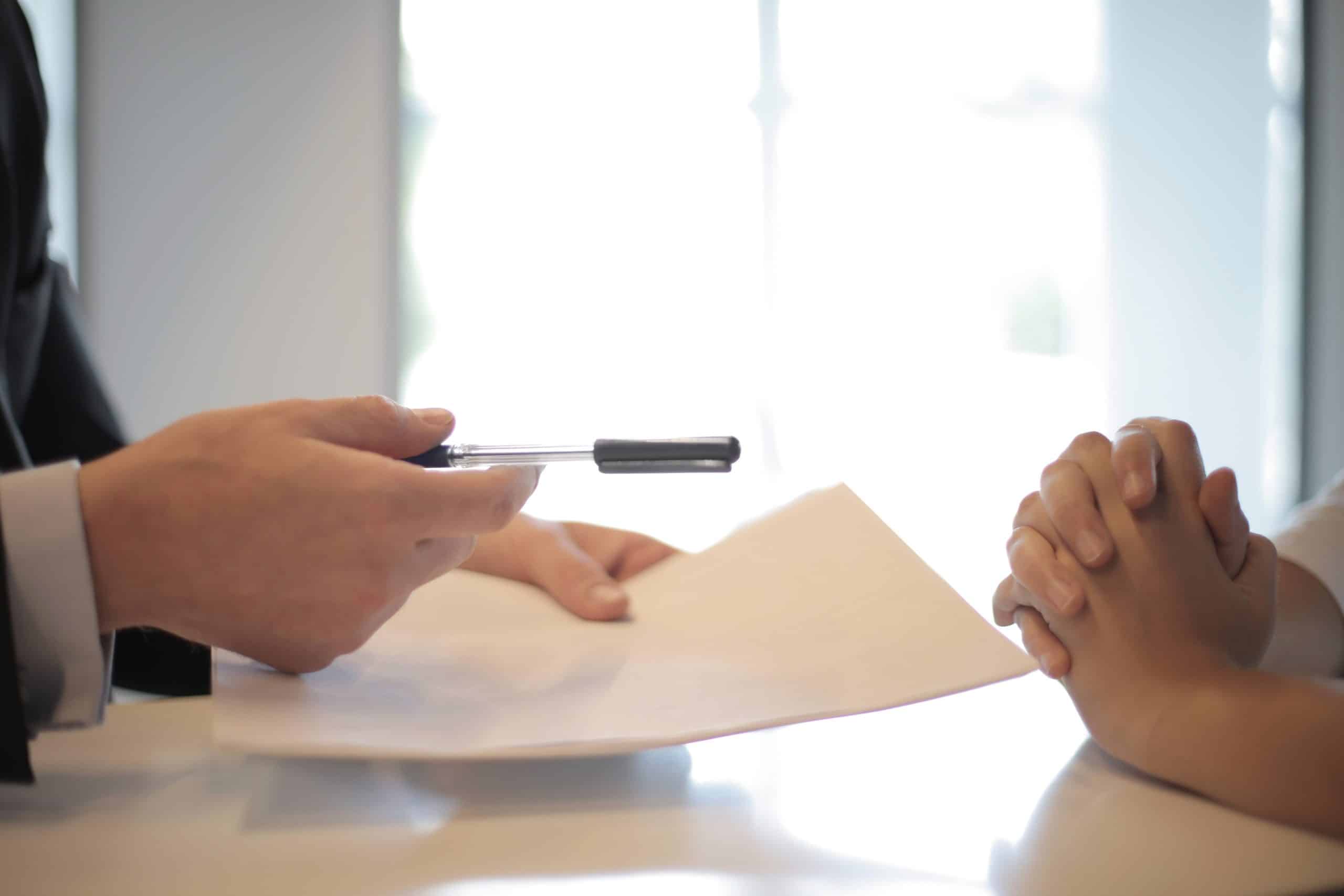 person handing a pen and document to another person