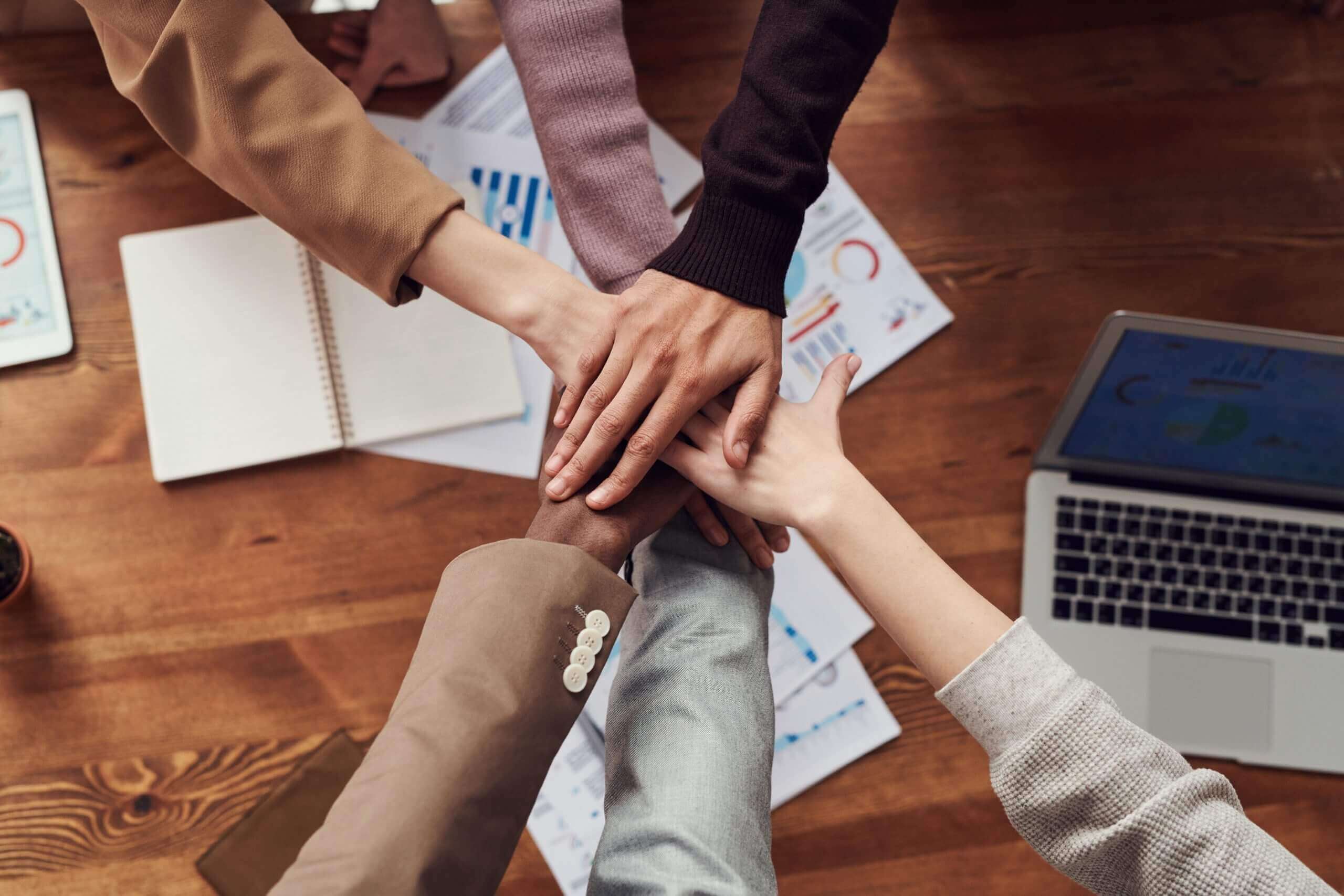 group of hands on top of one another over a wooden table